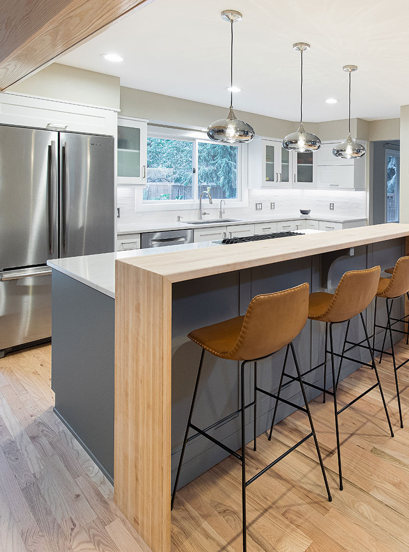 A modern kitchen with a white oak waterfall bar height countertop with leather barstools and shiny modern pendant lights in Fort Collins, Colorado