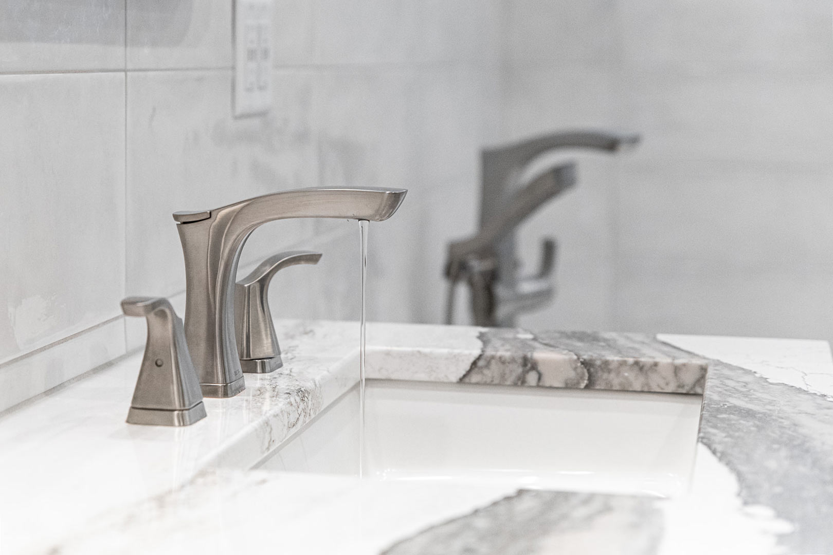 Detail image of a contemporary stainless steel faucet and a marble waterfall countertop