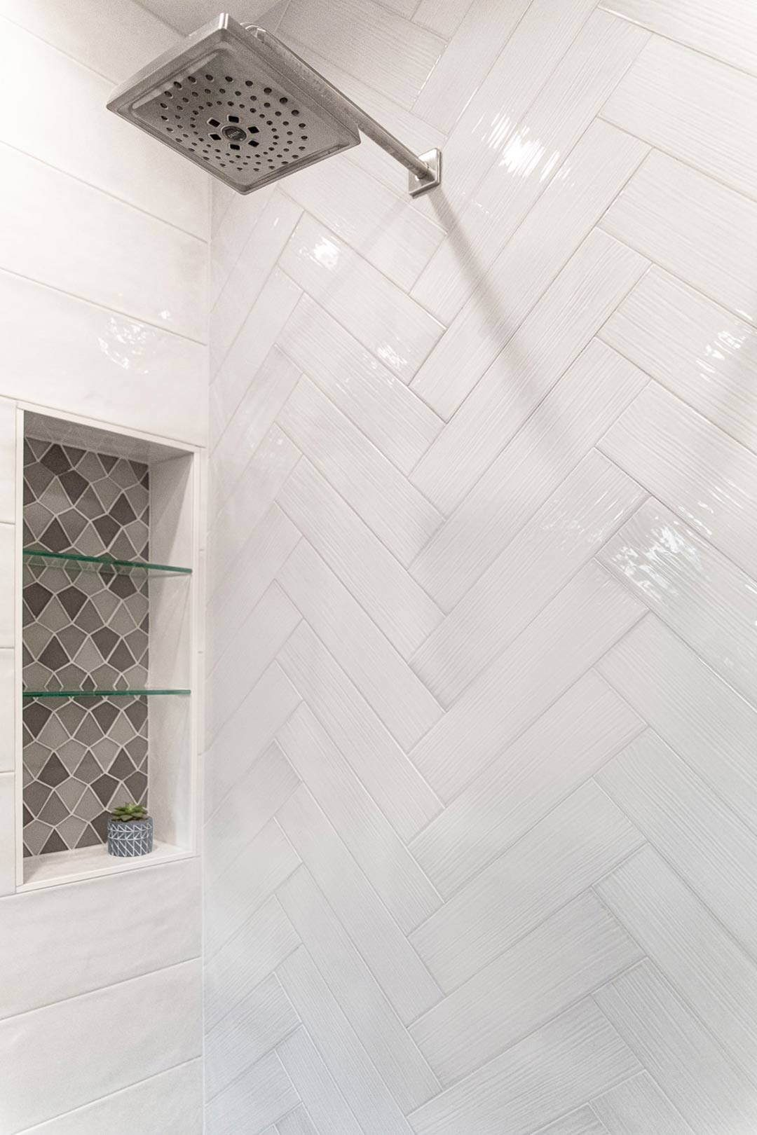 Herringbone accent wall and custom tiled shower niche installed in-house by Freestone Design-Build