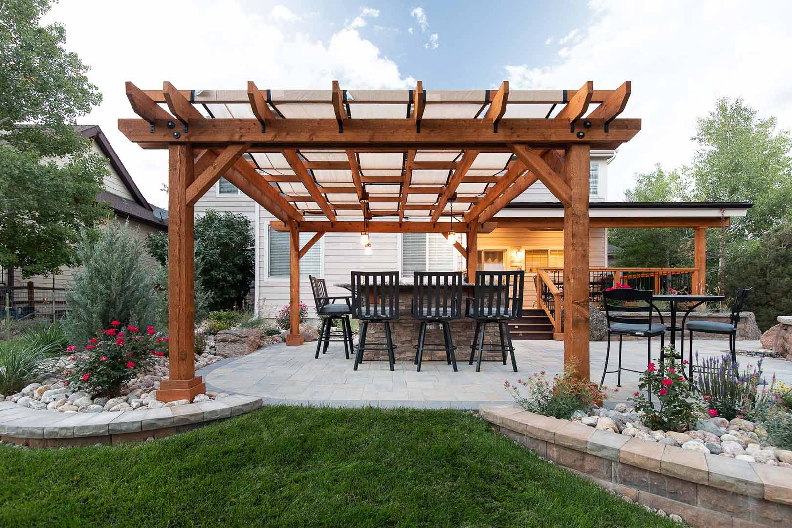 A large modern pergola with a five top bar nestled underneath on top of a custom paver patio. 