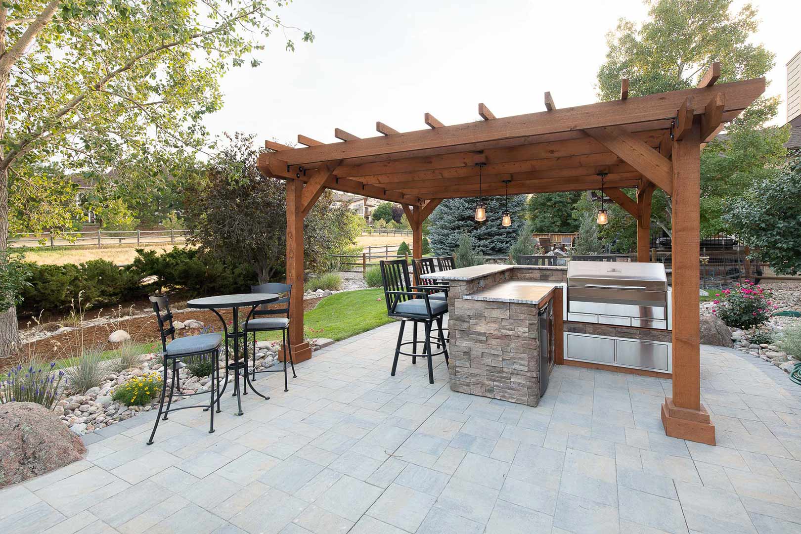 A wide angle view of the large paved patio and modern pergola with a built in grill and bar made from stacked stone.