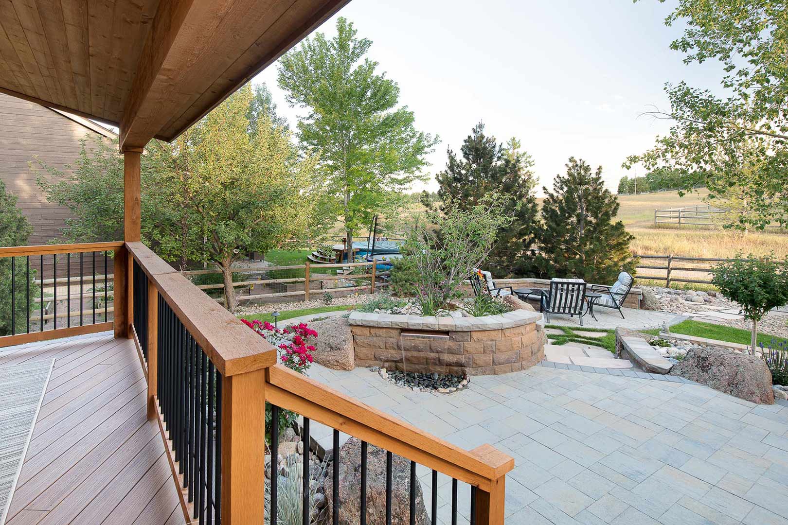 View from the covered patio looking down at the paved stone patio and built in water feature and fire pit designed by Freestone Design-Build.