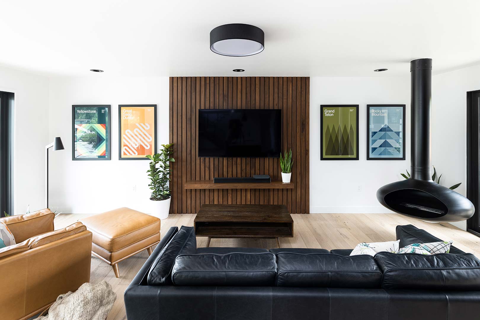 A wide angle view of the mid-century modern remodel of the living room that has a custom built wood slat accent wall panel that back the TV and has a built in shelf that was completed in-house by Freestone Design-Build.