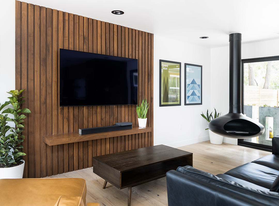 A living room of a whole home renovation by Freestone Design-Build with a wood slat custom feature wall behind the wall mounted tv with a built in floating shelf and mid-century furniture.