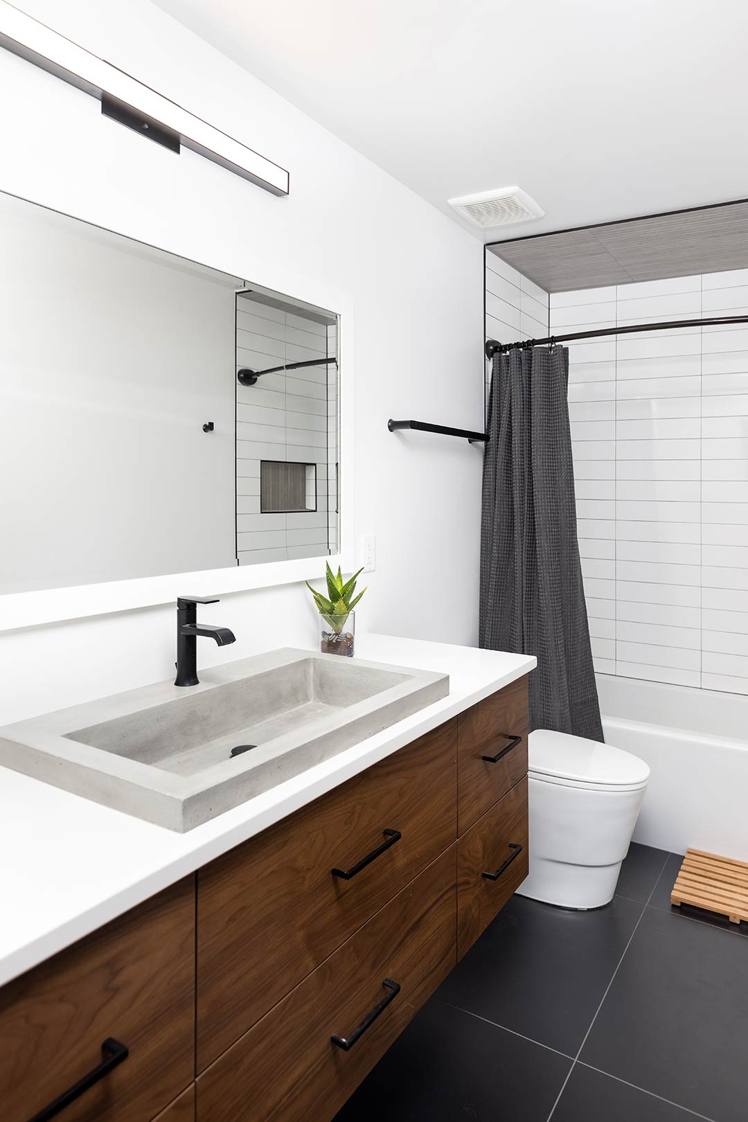 The upstairs hallway bath of this mid-century modern remodel features a custom vanity and concrete-look sink that ties into the rest of the aesthetic pulled together by Freestone Design-Build
