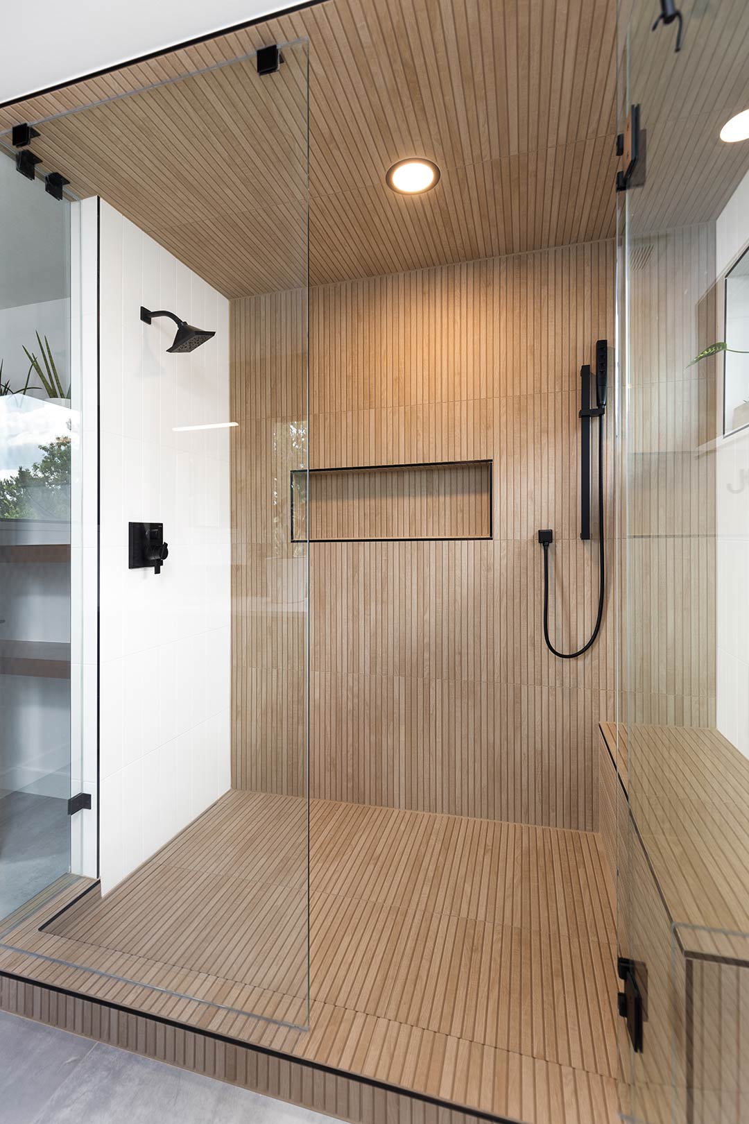 A gorgeous walk-in shower with wood slat-look tile with can lighting and a custom shower niche with a built in bench installed in-house by Freestone Design-Build