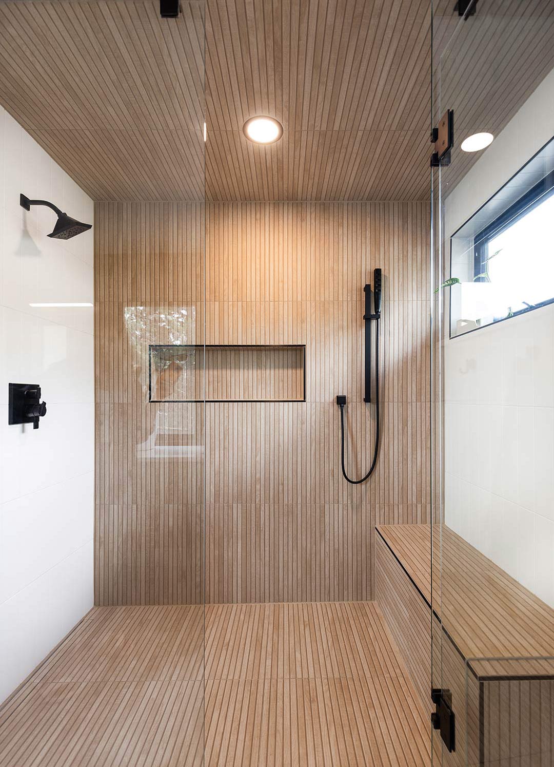 Custom tiled luxury walk-in shower with wood-slat-look tile, a built-in bench, recessed can light, and matte black fixtures designed and installed by Freestone Design-Build