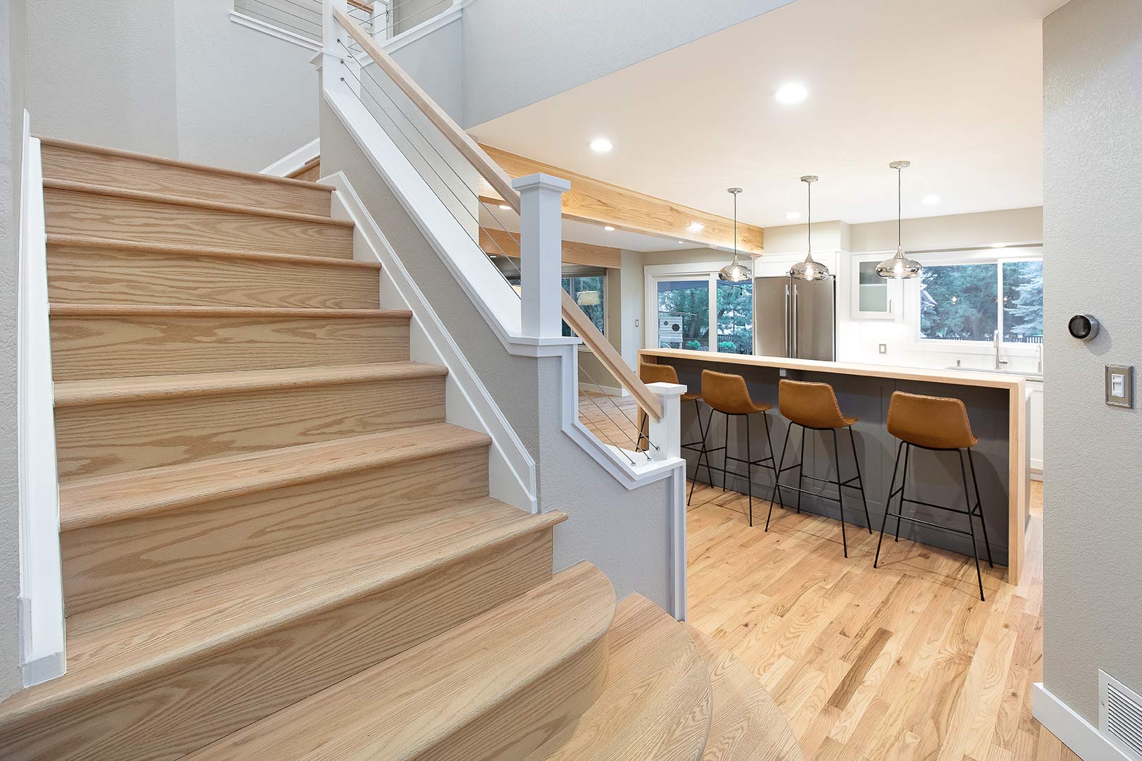 Detailed image showing the juxtaposition of the stunning white oak staircase with the white oak waterfall counter and barstools of the kitchen in the background. 