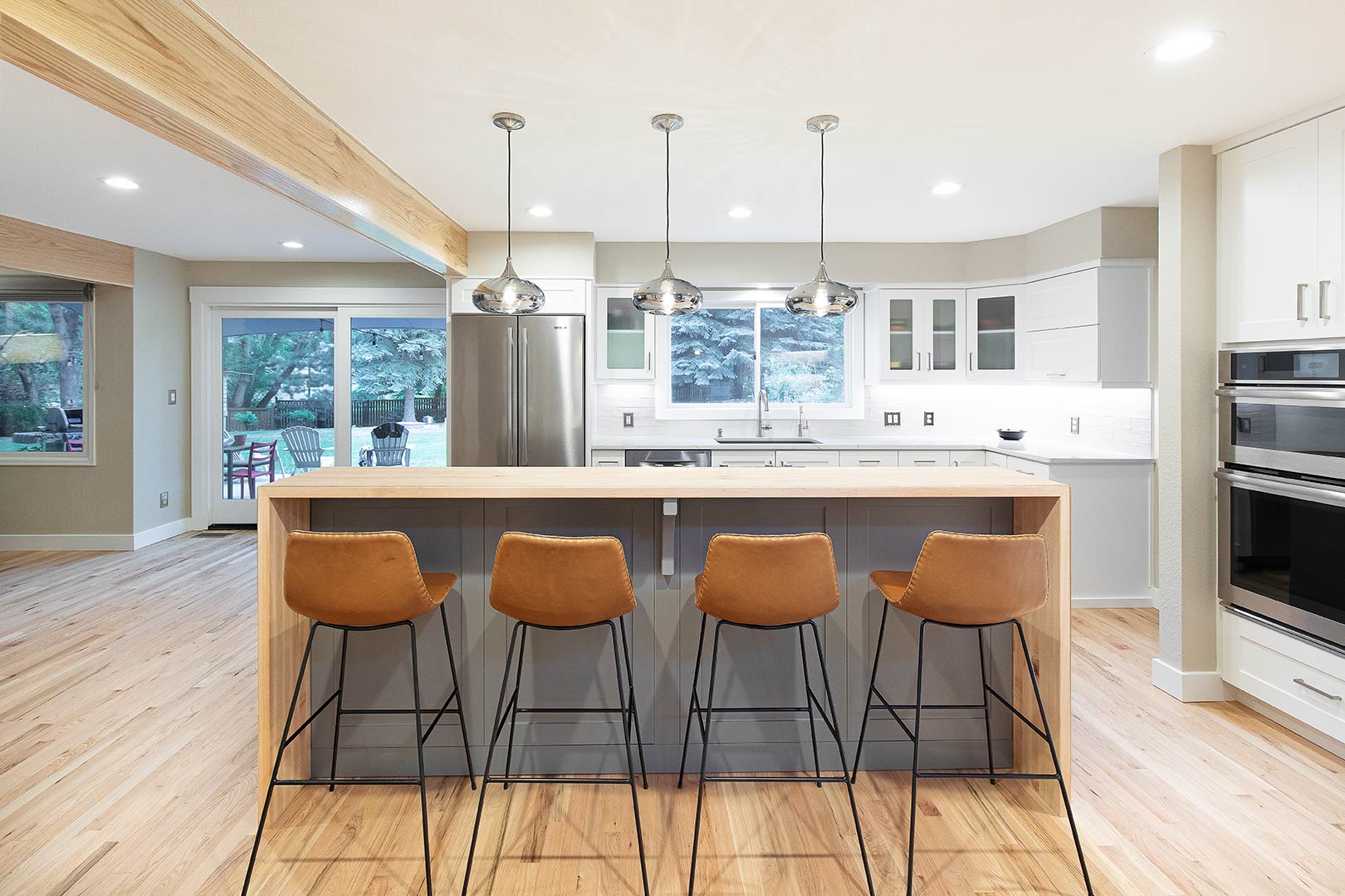 Straight on view of the back of the four modern leather barstools nest under the bar height waterfall white oak countertop designed by Freestone Design-Build. 