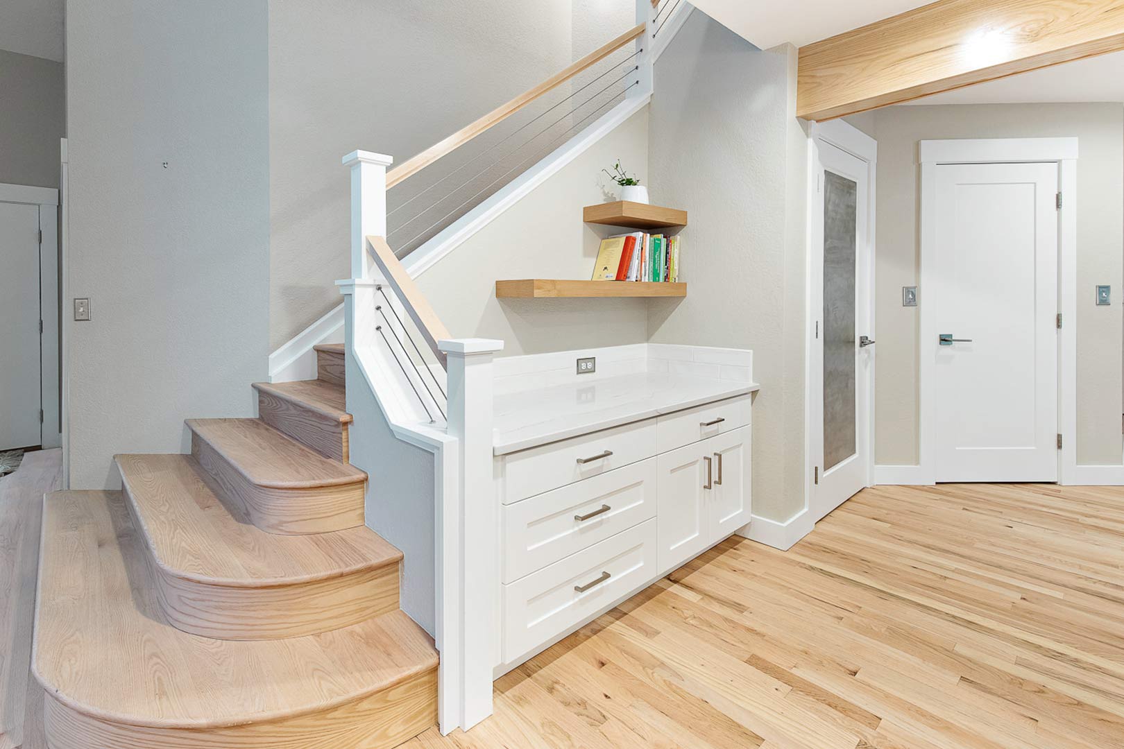 A white oak staircase with a custom built handrail made from white oak and cable matches the aesthetic of the transitional modern kitchen design