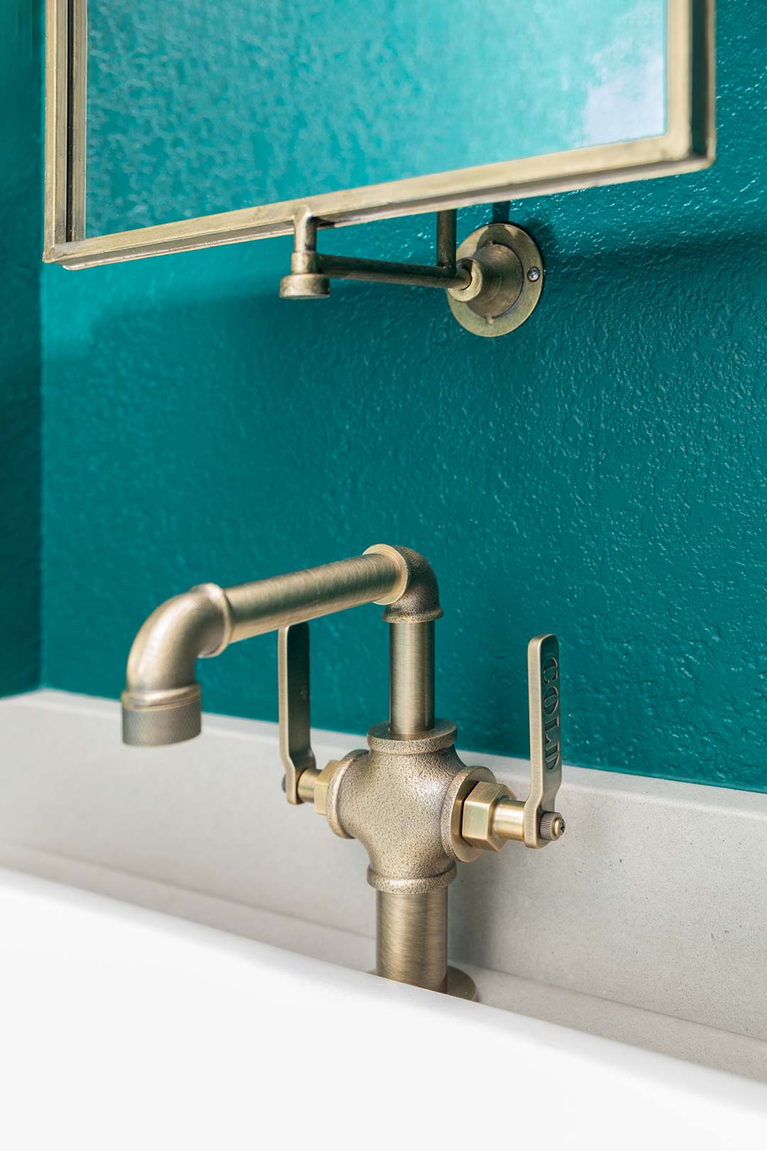 Unique plumbing fixture featured in the powder bath that is brass and matches the vanity mirror installed above it.