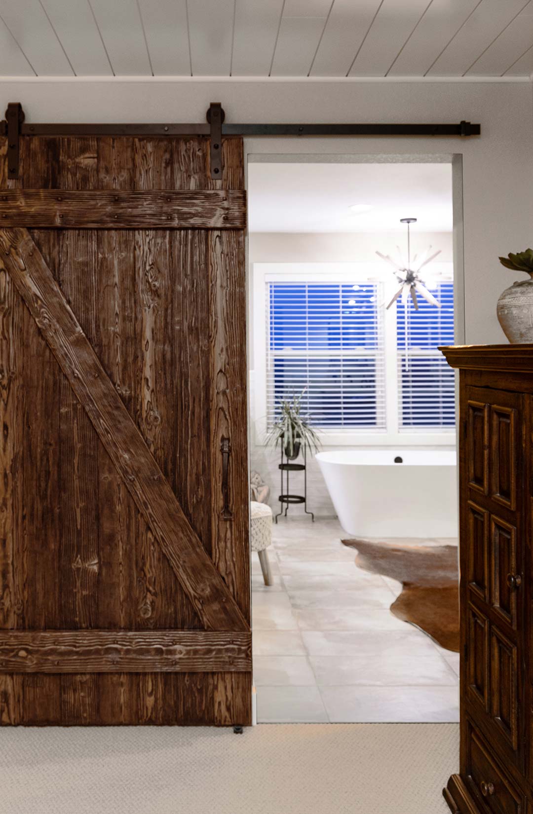 Custom dark stained barn wood sliding door with a glimpse into the primary renovated bathroom