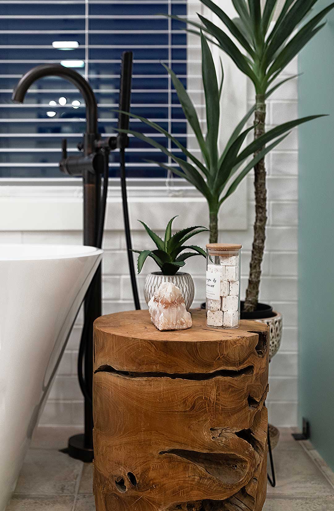 Detailed view of a natural wood stool with bath soaps and plants next to the modern faucet and freestanding tub 