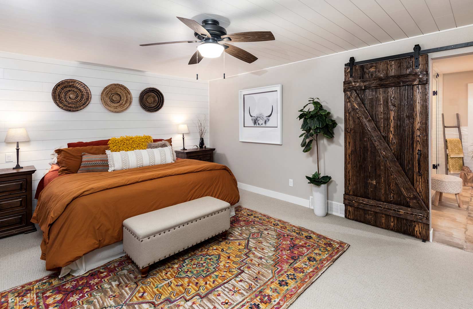 Primary bedroom with warm bohemian colors and dark wood tones with a featured barn wood sliding door created by Freestone Design-Build.