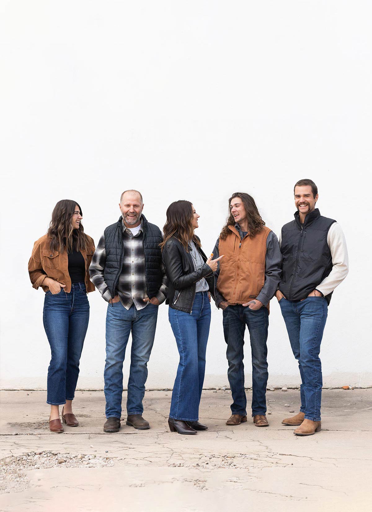 The Freestone Design-Build team stands in front of white wall in Old Town Fort Collins with on-brand outfits and they are all laughing and talking with each other