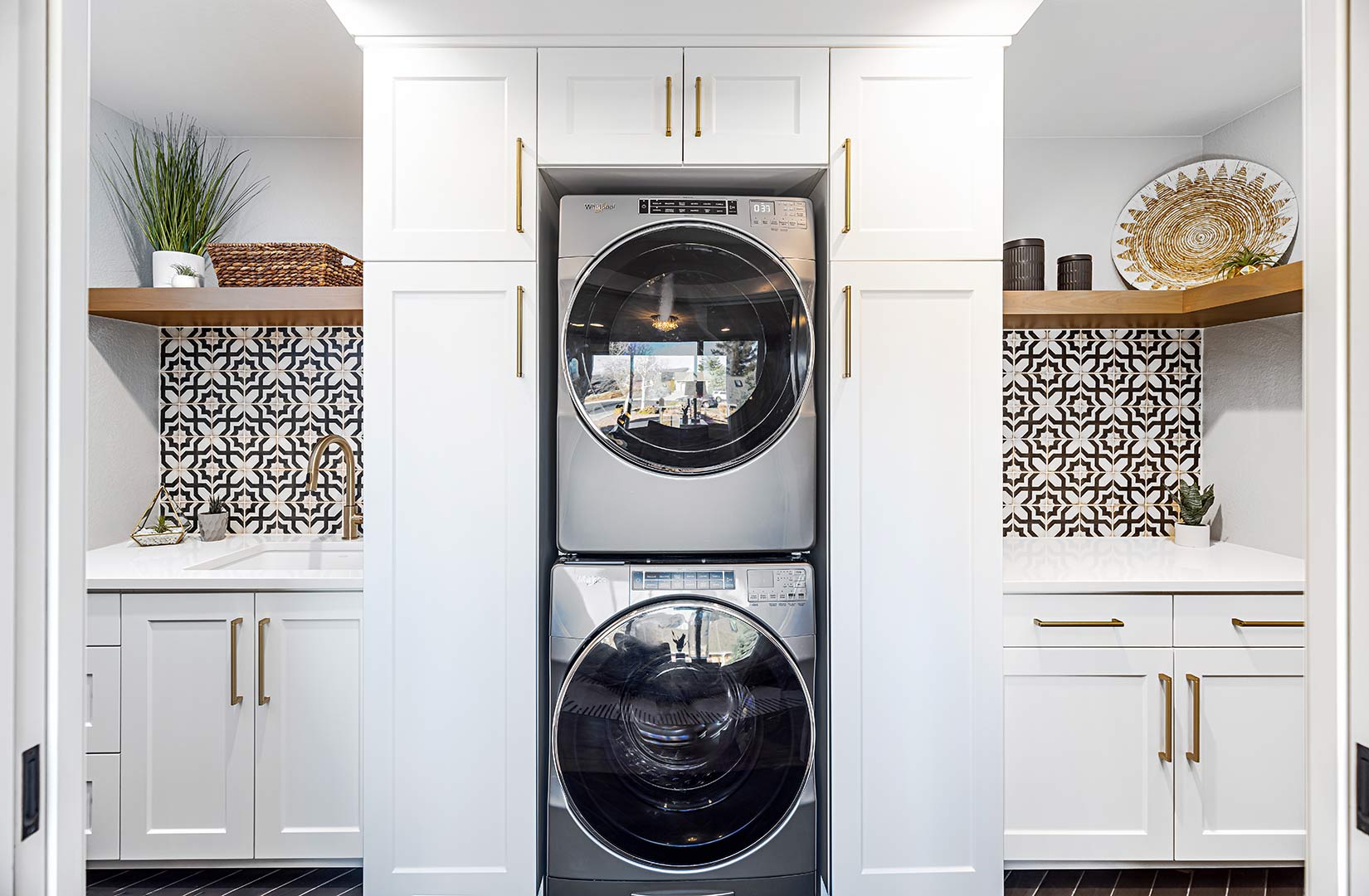 Modern laundry addition showing white built-in cabinets with stacked washer and dryer with brass pulls. 