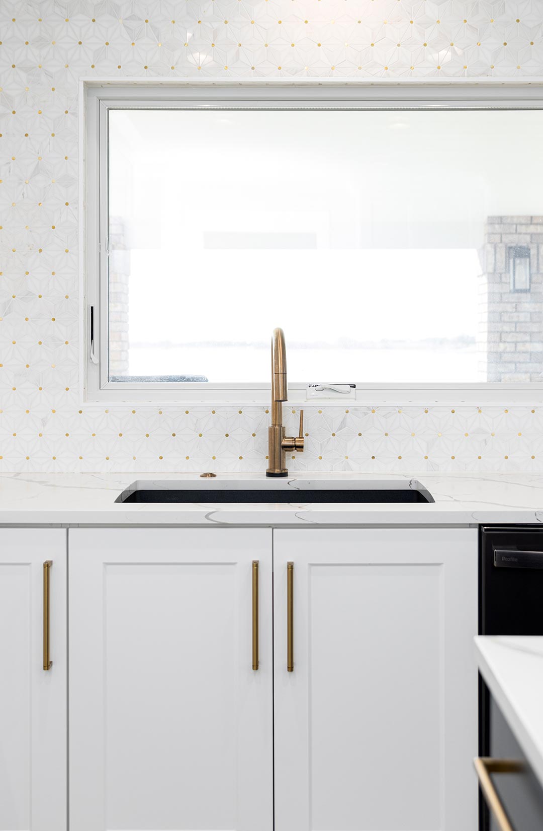 The sink of Janna Drive's kitchen showing a brass faucet under a large open window