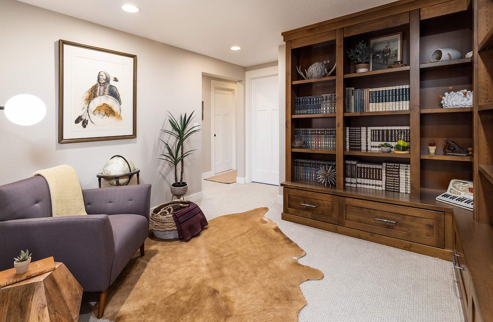 Built in bookcases and a large accent chair with a cow skin rug show the styled library by Freestone Design-Build. 