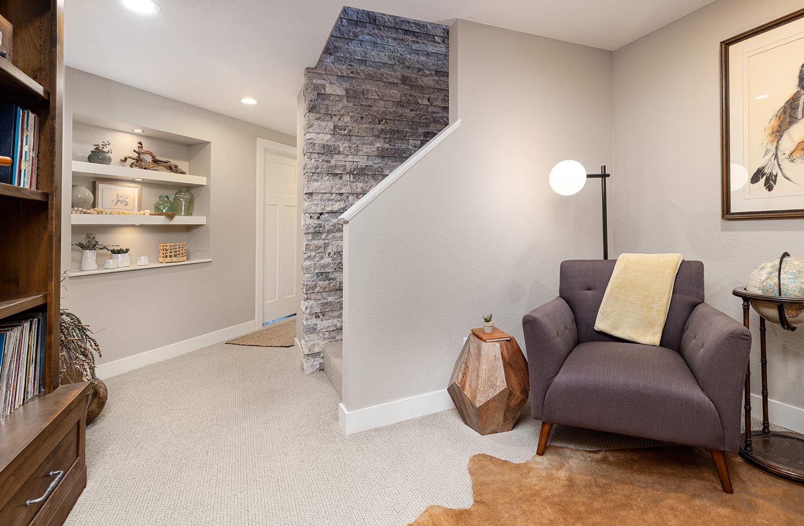 Downstairs library at the landing of the stairs shows a rock wall that scales the two stories of this renovated home